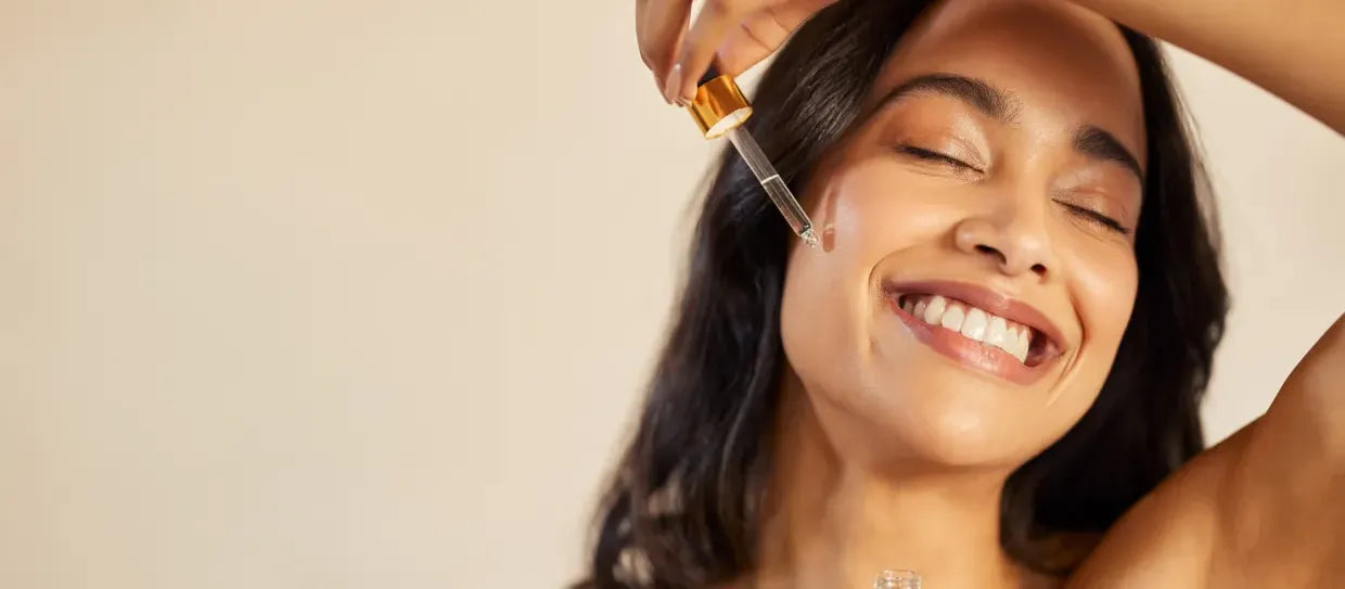 A woman applying face serum to reduce hyperpigmentation on her cheeks, showcasing a glowing complexion.