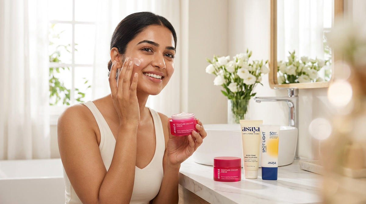 A smiling young indian woman applying skincare in a bright, minimal bathroom, holding a premium skincare set on a clean vanity, soft natural lighting, fresh glowing skin, elegant and aesthetic. 