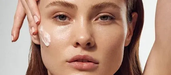 A woman applying sunscreen on her face, focusing on hydration for dehydrated skin in sunny weather.