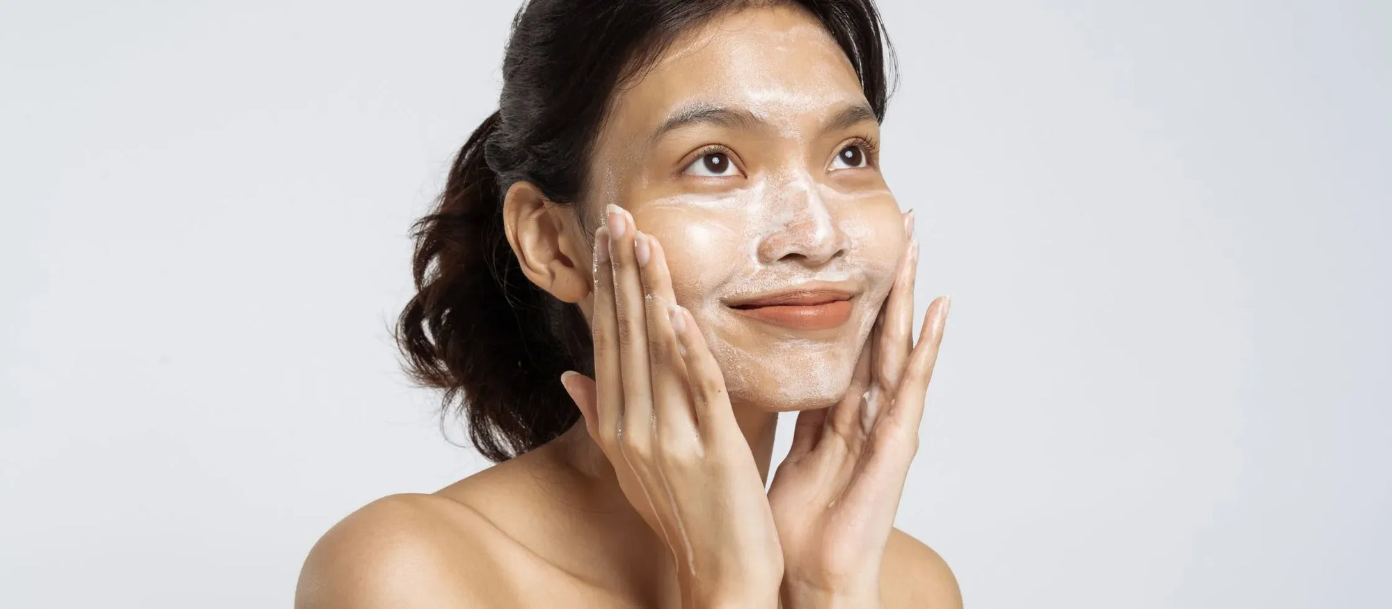 A woman examining different acne face washes for dry skin in a bright bathroom setting.