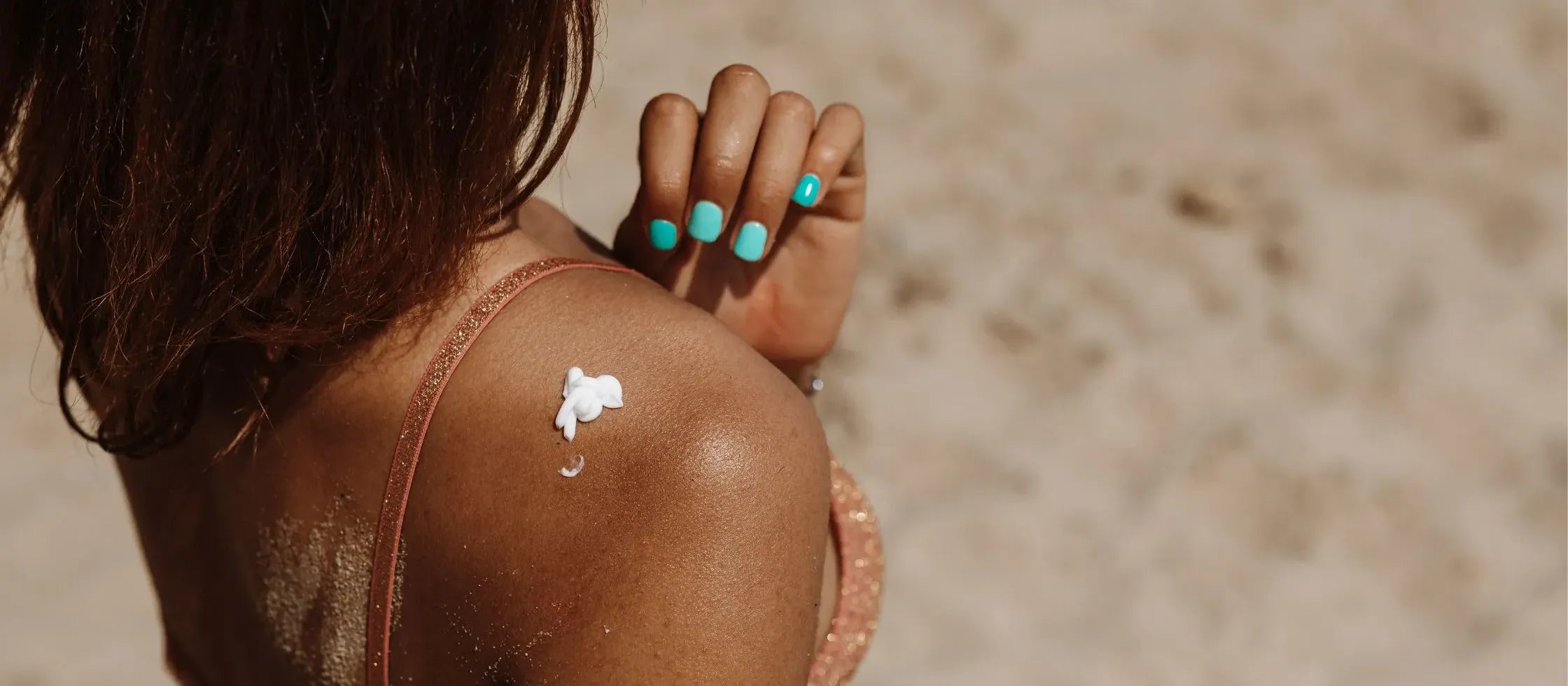 A bottle of gentle sunscreen for sensitive skin on a beach, surrounded by sun hats and sunglasses.