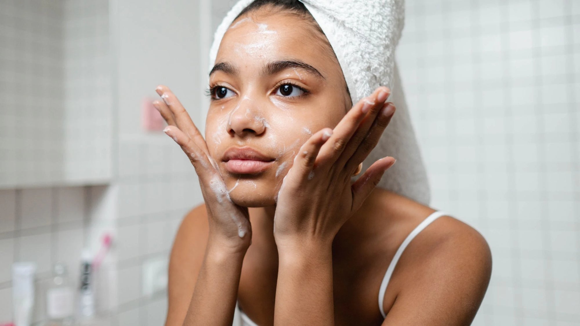 A woman examining her face in the mirror, focusing on an uneven skin tone and dark spots. 